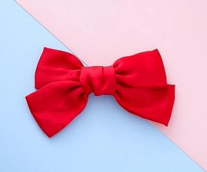 Detail of red satin bow hair clip with a smooth glossy finish on a pastel background