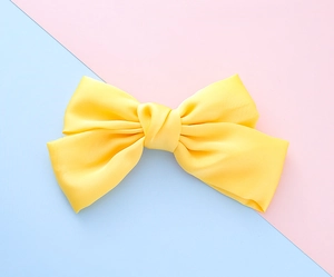 Close-up of bright yellow fabric bow hairclip with satin texture on pink and blue background