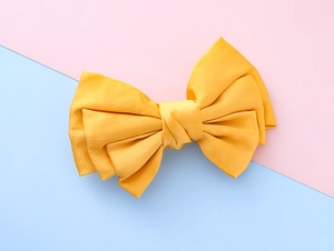 Detailed view of layered large yellow satin bow hair clip on a pink and blue background