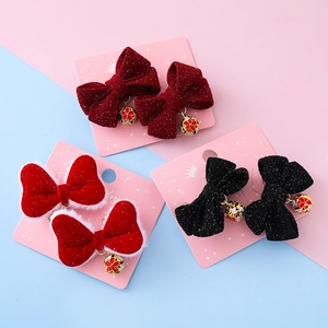 Three pairs of festive red bow hair clips with golden floral bell pendants on a card