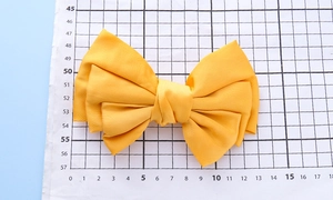 Macro shot of large yellow handmade fabric bow hair clip on a measuring scale ruler