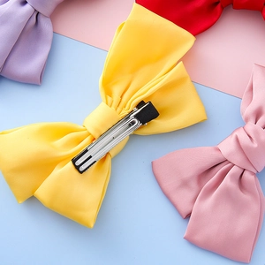 Handmade large satin bow hair clip for girls featuring a yellow fabric and a metal duckbill clip
