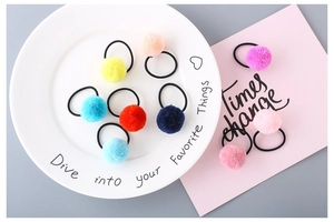 Flat lay of colorful plush ball hair ties in various candy colors on a white ceramic plate
