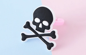 Dettaglio dell'anello in PVC morbido con teschio e ossa su sfondo rosa tenue