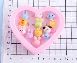 Close-up of kids cartoon resin rings in a pink heart box featuring animal and fruit shapes