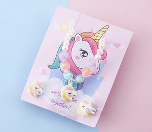 Dettaglio di un set di gioielli con unicorno in resina su cartoncino rosa e perline