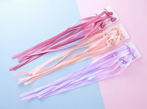 Détail de pinces à cheveux nuds en satin avec de longs pompons roses et violets