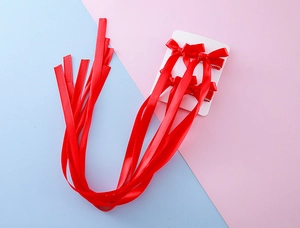 Détail de quatre barrettes à nœuds en satin rouge avec de longs rubans sur carte
