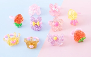 Dettaglio di anelli per bambini in resina glitterata con forme di fragola e corona