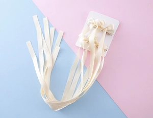 Détail d'une paire de barrettes à nœuds en satin crème avec de longs rubans sur carte