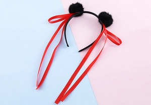 Dettaglio di un cerchietto con pompon neri e lunghi nastri rossi per capelli
