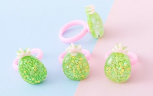 Dettaglio di graziosi anelli per bambini in plastica rosa con ciondoli ananas glitterati