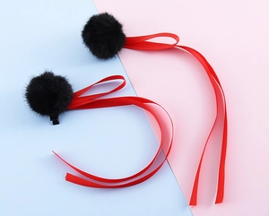 Dettaglio di fermagli per capelli con pompon neri e lunghi nastri di raso rosso e base in metallo