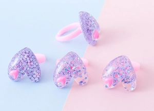 Dettaglio di anelli a cuore in resina colorata per bambine con glitter e fascia regolabile