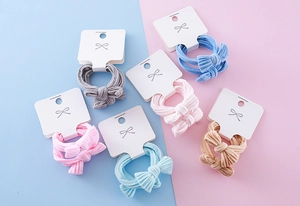 Close-up of six colorful bow hair ties with soft ribbed texture on display cards