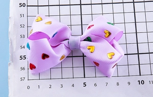 Detailed close-up of a light purple grosgrain hair bow with colorful foil hearts