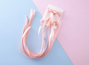 Détail de quatre barrettes nœuds en satin rose avec longs rubans sur carte blanche
