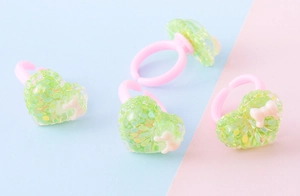 Dettaglio di anelli a forma di cuore in resina rosa e verde con glitter per bambini