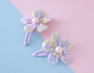 Detail showing two purple floral hair clips with sequins and a pearl center on pastel background