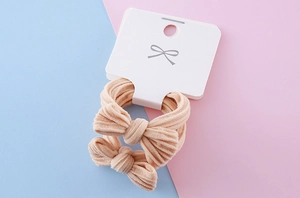 Macro detail of beige ribbed fabric bow hair ties on a minimalist display card