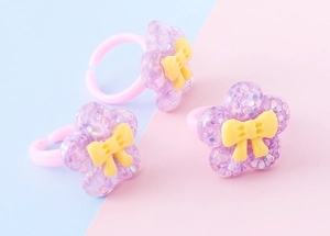 Dettaglio di anelli per bambini in resina con fiori viola glitterati e fascia rosa