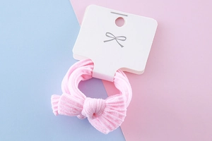 Detail of pink bow hair tie with textured fabric on white display card for kids