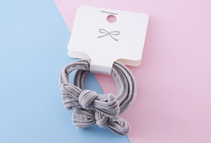 Detail view of two grey bow-knot elastic hair ties displayed on a white branded card