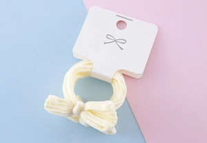 Detail of light yellow bow hair tie with striped velvet texture on display card