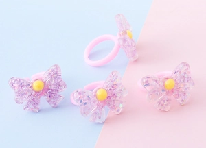 Dettaglio di anelli per bambini a forma di fiocco in resina con glitter su sfondo colorato