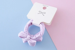 Close-up of lavender bow hair tie with ribbed texture on pastel blue and pink background