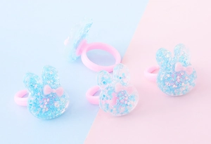 Anelli per bambini con coniglietto di paillettes blu e fiocco rosa su fascia in plastica