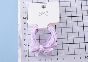 Detail of lavender ribbed bow hair tie on white display card with grid background