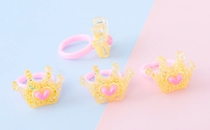 Dettaglio di quattro anelli per bambini in resina con corone glitterate e cuori rosa