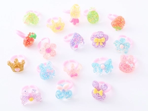 Dettaglio di anelli in resina glitterata per bambini con forme di fragola e corona