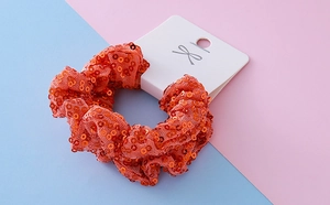Detail of orange sequined Halloween scrunchie on white display card with bow logo