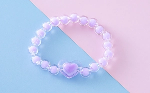 Primer plano de una linda pulsera de cuentas moradas con dije de corazón y cuentas acrílicas