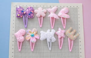 Set mit neun bunten Kinder-Haarspangen mit Bogen-, Bär- und Kronenmotiven auf einem Gitter