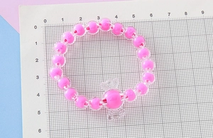 Detalle de pulsera de cuentas rosas con dije de caramelo sobre una rejilla de medida