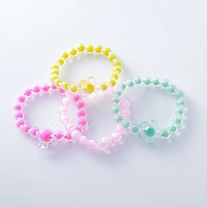 Detalle de cuatro pulseras de cuentas acrílicas de colores con dijes de flores para niños
