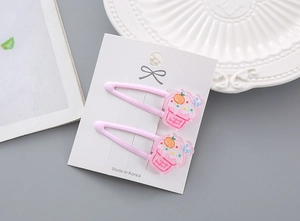 Vue détaillée de deux barrettes roses en forme de glace et cupcake sur une carte d'exposition