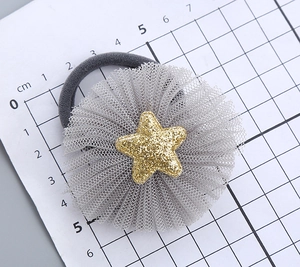 Macro shot of gray tulle flower hair tie with gold glitter star detail on scale background