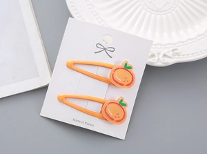 Gros plan de deux pinces à cheveux orange avec décorations de fruits sur carte blanche