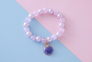 Detail of beaded bracelet featuring purple faux pearls, crackled beads and shell charm