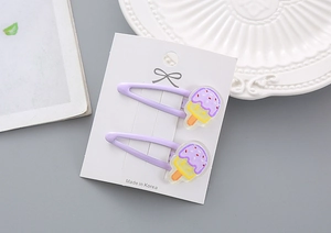 Gros plan de deux pinces à cheveux crème glacée violettes sur carton avec assiette