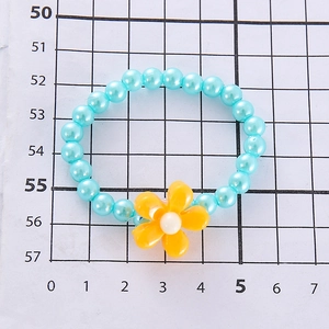 Detail view of blue beaded children's bracelet with a yellow flower charm on grid background