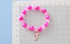 Detailed shot of girls beaded bracelet with pink crackle beads and seahorse charm