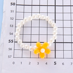 Close-up of a white faux pearl bracelet with a bright yellow flower charm on grid paper