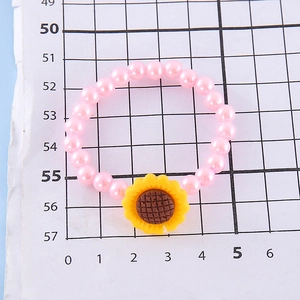 Close-up of pink beaded bracelet with yellow sunflower charm on white grid paper