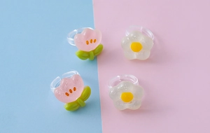 Dettaglio di anelli trasparenti regolabili in resina per bambini con fiori glitterati