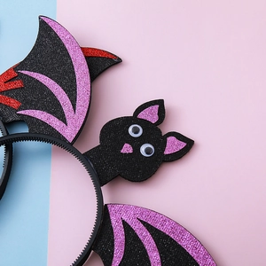 Halloween bat wing headband with glitter patterns and wiggle eyes on a bicolor background